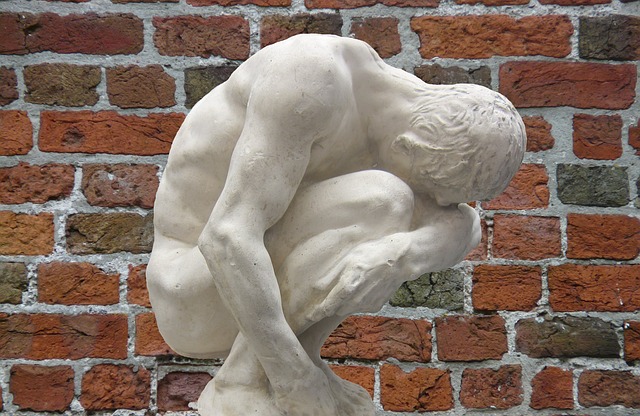 Burn-out représenté par une statue recroquevillée devant un mur de briques rouges